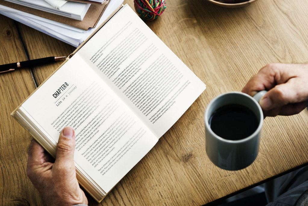 Persona leyendo un libro con una taza de café en la mano