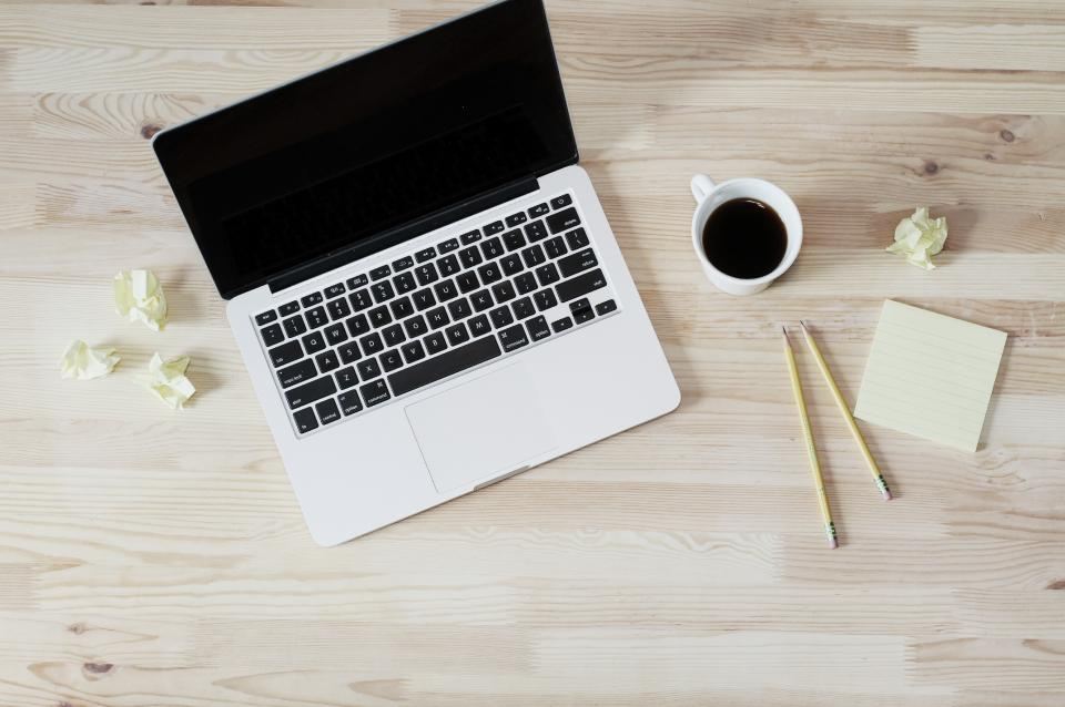 Taza de café junto a un computador portátil sobre una mesa de madera