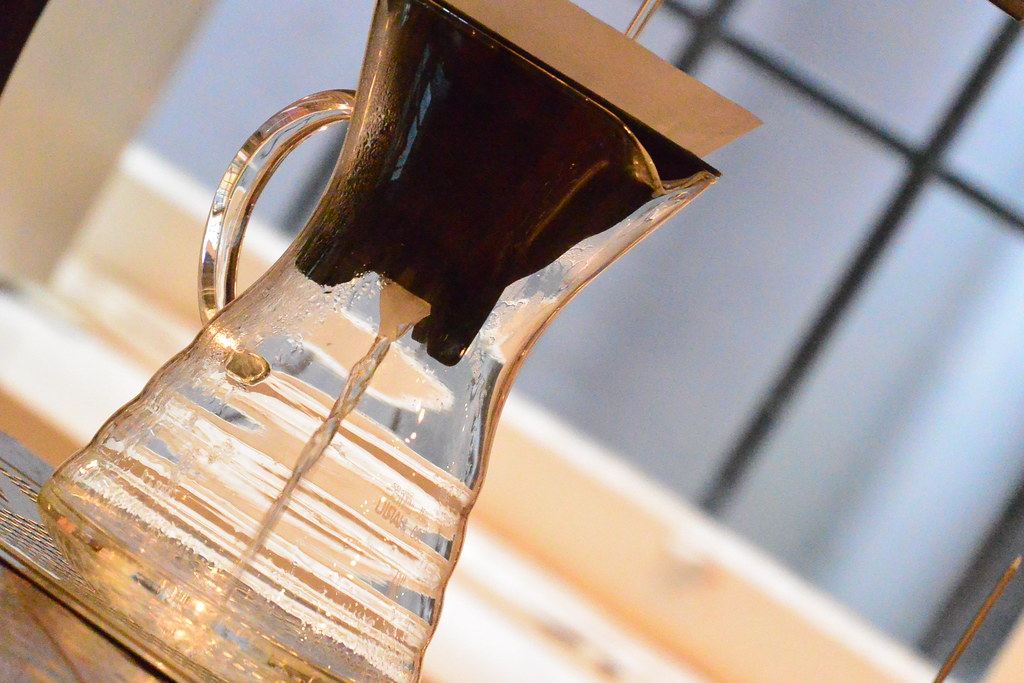 Café pasando por un filtro de papel hacia una jarra de vidrio junto a una ventana