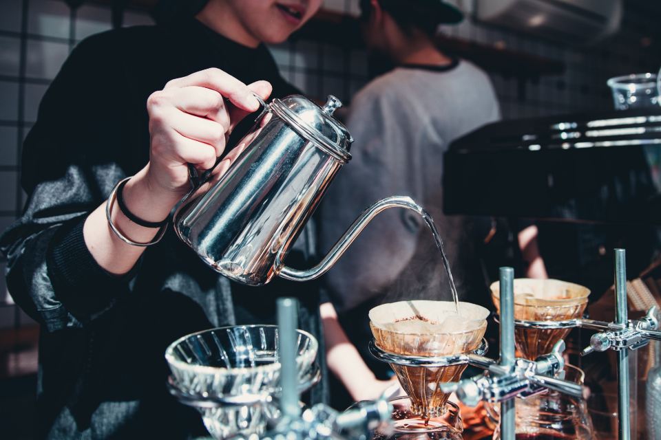 Barista vertiendo agua con una tetera de cuello de cisne sobre café filtrado